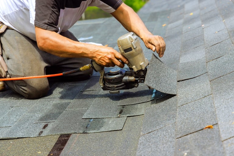Roofer using pneumatic nail gun during shingle installation